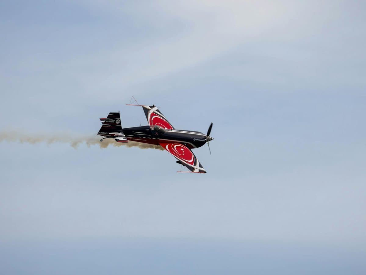 Red aerobatic airplane banking in flight with a smoke trail